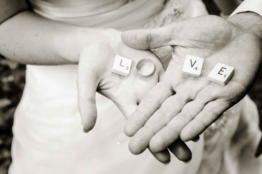 Handen van vers getrouwd koppel met de Scrabble letters die het woord love vormen in de hand
