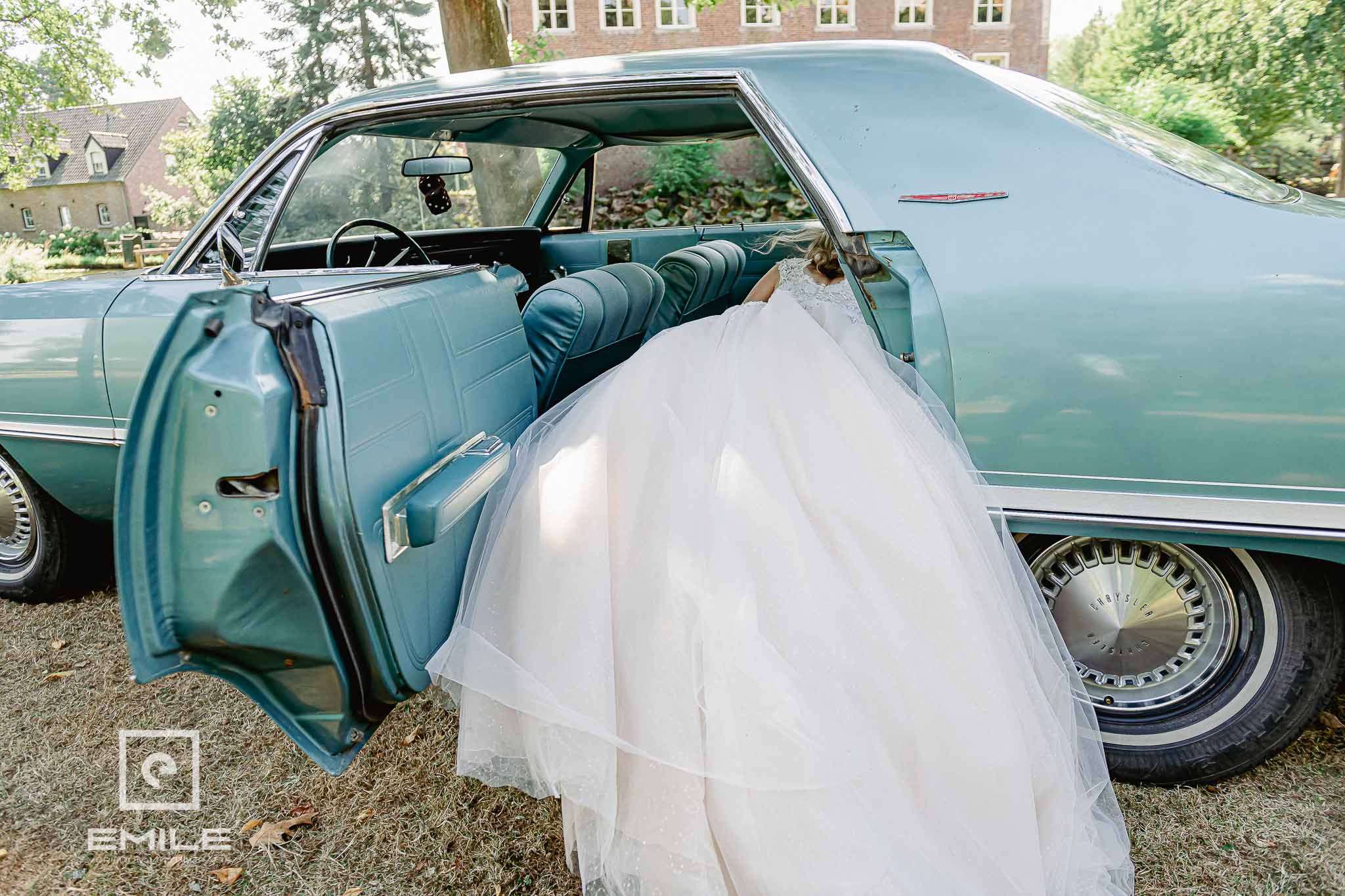 Bruid hangt met de benen uit de old timer bruidsauto bij het kasteel - trouwfotograaf Limburg Emile Verhijden